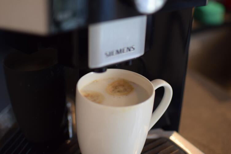Weiße Tasse mit frisch zubereitetem Kaffee unter einer Kaffeemaschine.