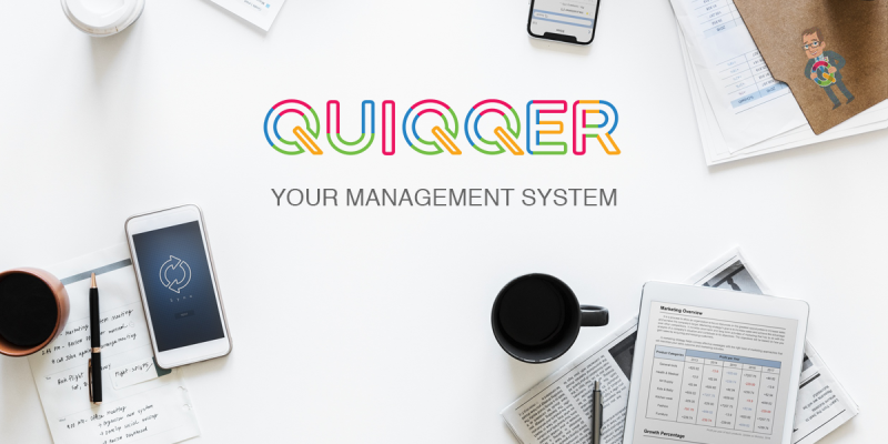 Release: QUIQQER 2 QUIQQER-Schriftzug auf einem hellen Schreibtisch mit Laptop, Telefon und Unterlagen.
